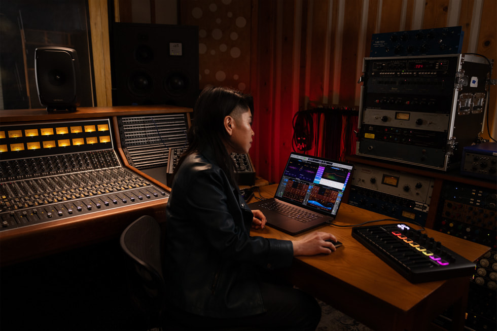 A person works in Logic Pro on a MacBook in a recording studio.